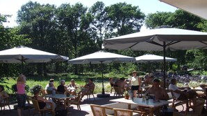 An outdoor patio area with tables and chairs under umbrellas, surrounded by greenery. - Farmhouse in Herperduin with Bubble Bath (Herpen)