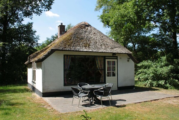 A small house with a thatched roof, a large window, and a door. There is a table with chairs outside. - Farmhouse in Herperduin with Bubble Bath (Herpen)