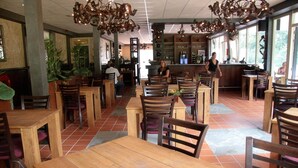 A restaurant interior with wooden tables and chairs, a bar area, and large windows allowing natural light. - Farmhouse in Herperduin with Bubble Bath (Herpen)