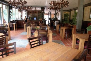 A restaurant with wooden tables and chairs, a bar area, and large windows allowing natural light. - Farmhouse in Herperduin with Bubble Bath (Herpen)