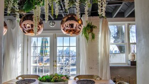 Un espace repas doté d’une grande table, de luminaires sphériques suspendus et offrant une vue sur la ville grâce à de larges fenêtres.