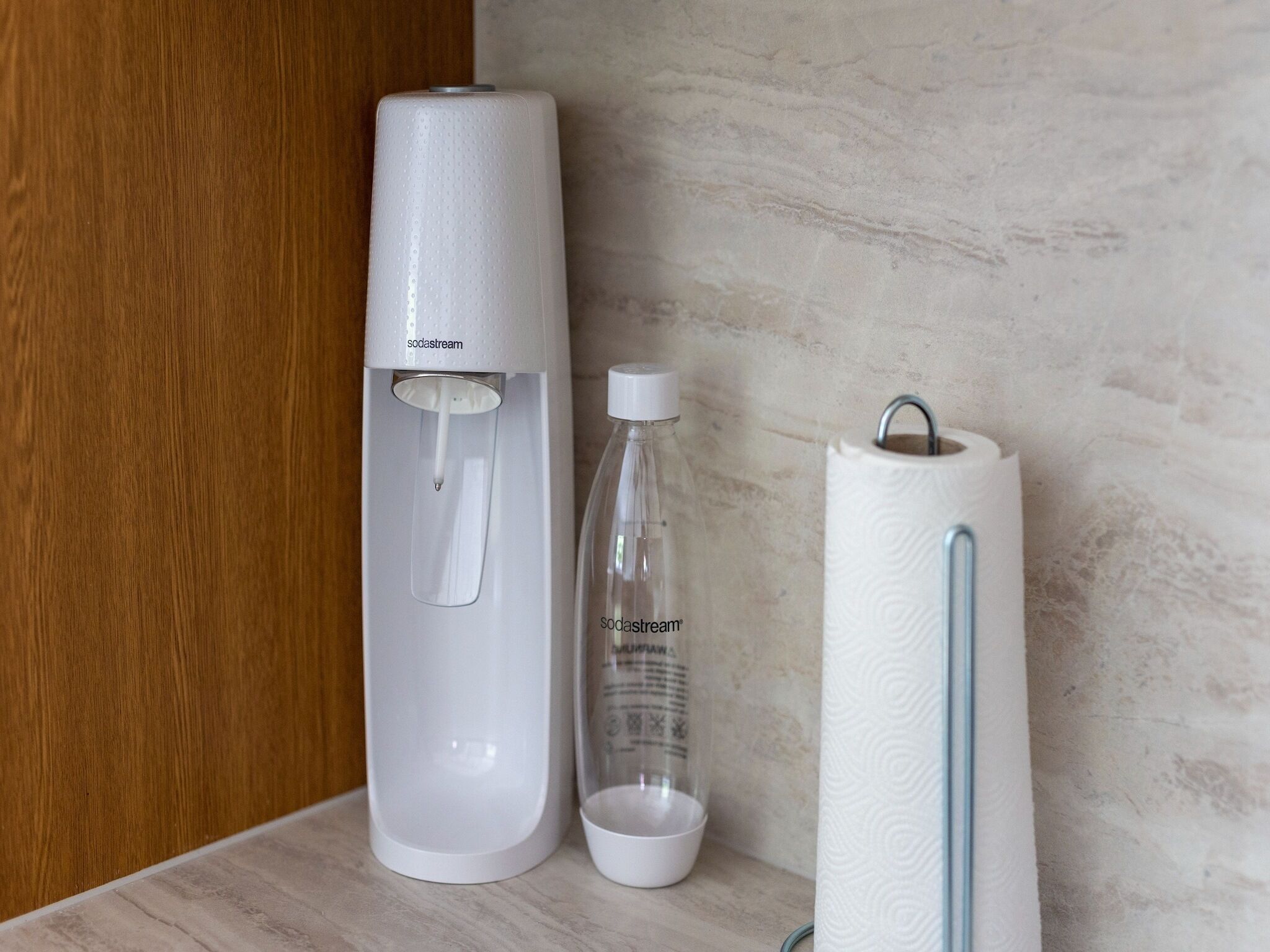A white water dispenser, a clear bottle with a label, and a white paper towel holder on a wooden surface.