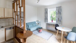 A modern kitchen with wooden cabinetry, a dining area with a round wooden table, and a blue sofa in a bright room with a window.