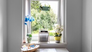 A window with a welcome sign, two potted orchids, a basket of cards, and a desk with a book.