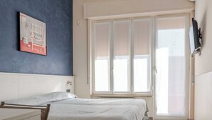 Ein Schlafzimmer mit Bett, Fenster mit Rollo, Heizkörper und einem Bild an der Wand.