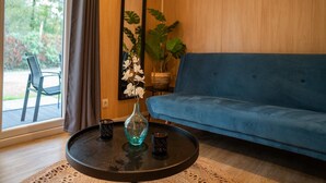 A room with a blue sofa, a round table with a vase and two cups, a mirror, and a potted plant.