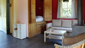 A cozy room with a wooden bed, a white sofa, a small table, and a wicker chair. - Cozy vacation home with terrace (Lage Zwaluwe)
