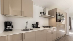Een moderne keuken met beige kastjes, een roestvrijstalen spoelbak, een koffiezetapparaat, een waterkoker en een fornuis.