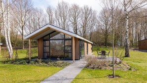 Een modern gebouw met grote ramen en een overdekte doorgang, omgeven door bomen en gras.