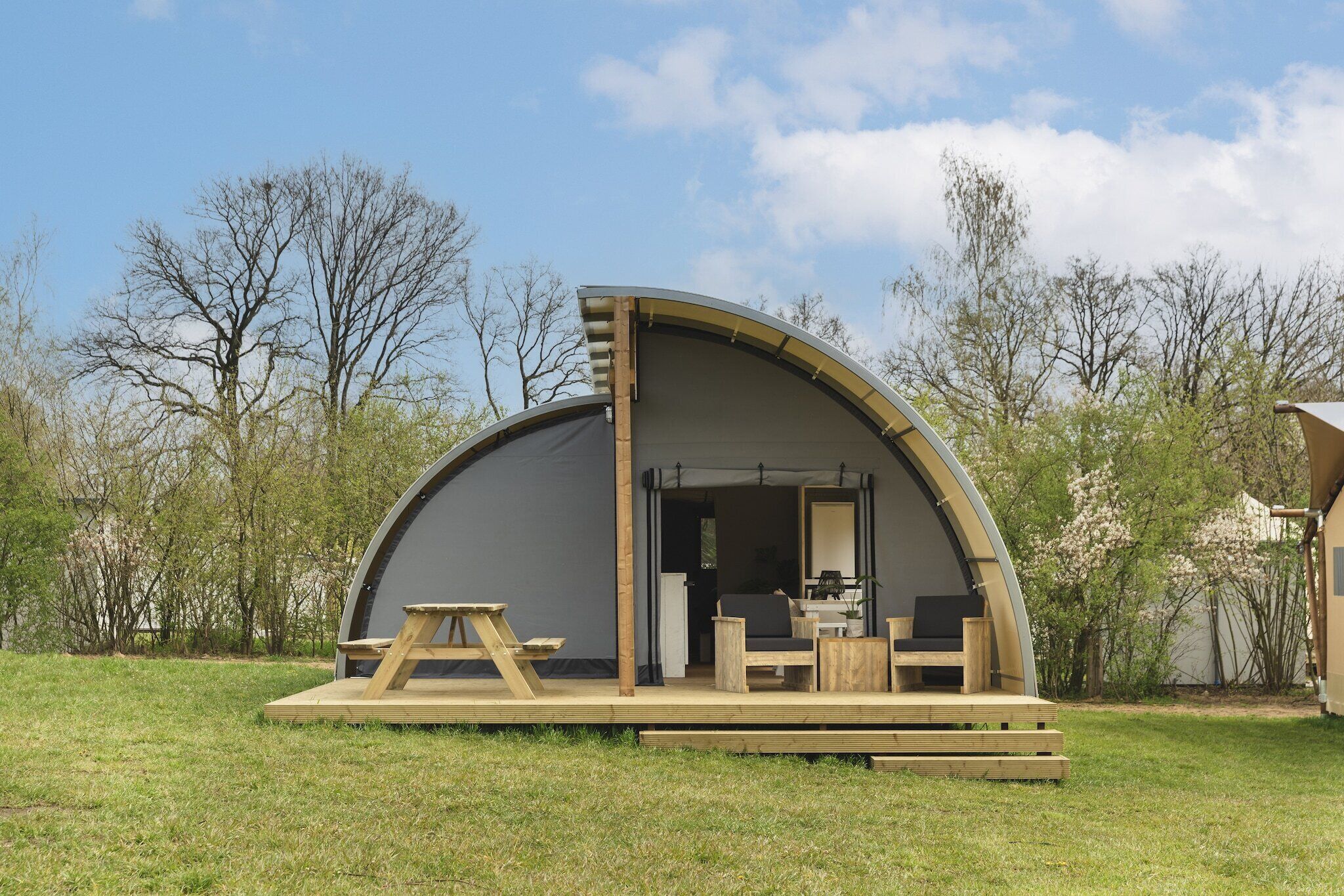 A semi-circular tent with a wooden deck, a table, and chairs.