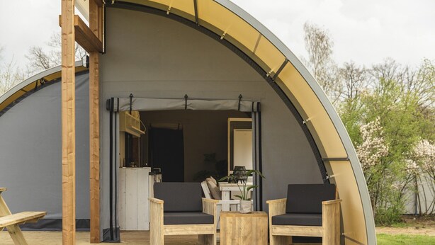A semi-open tent with a wooden deck, two chairs, a table, and a small kitchen area.
