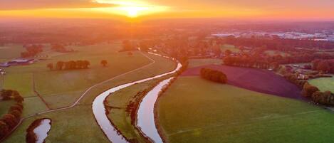 A rural landscape with fields, a winding water channel, and a sunset.