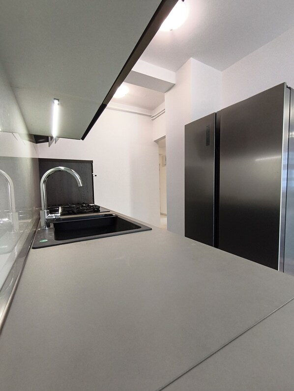 A modern kitchen with a stainless steel refrigerator, a black sink, and a sleek countertop.
