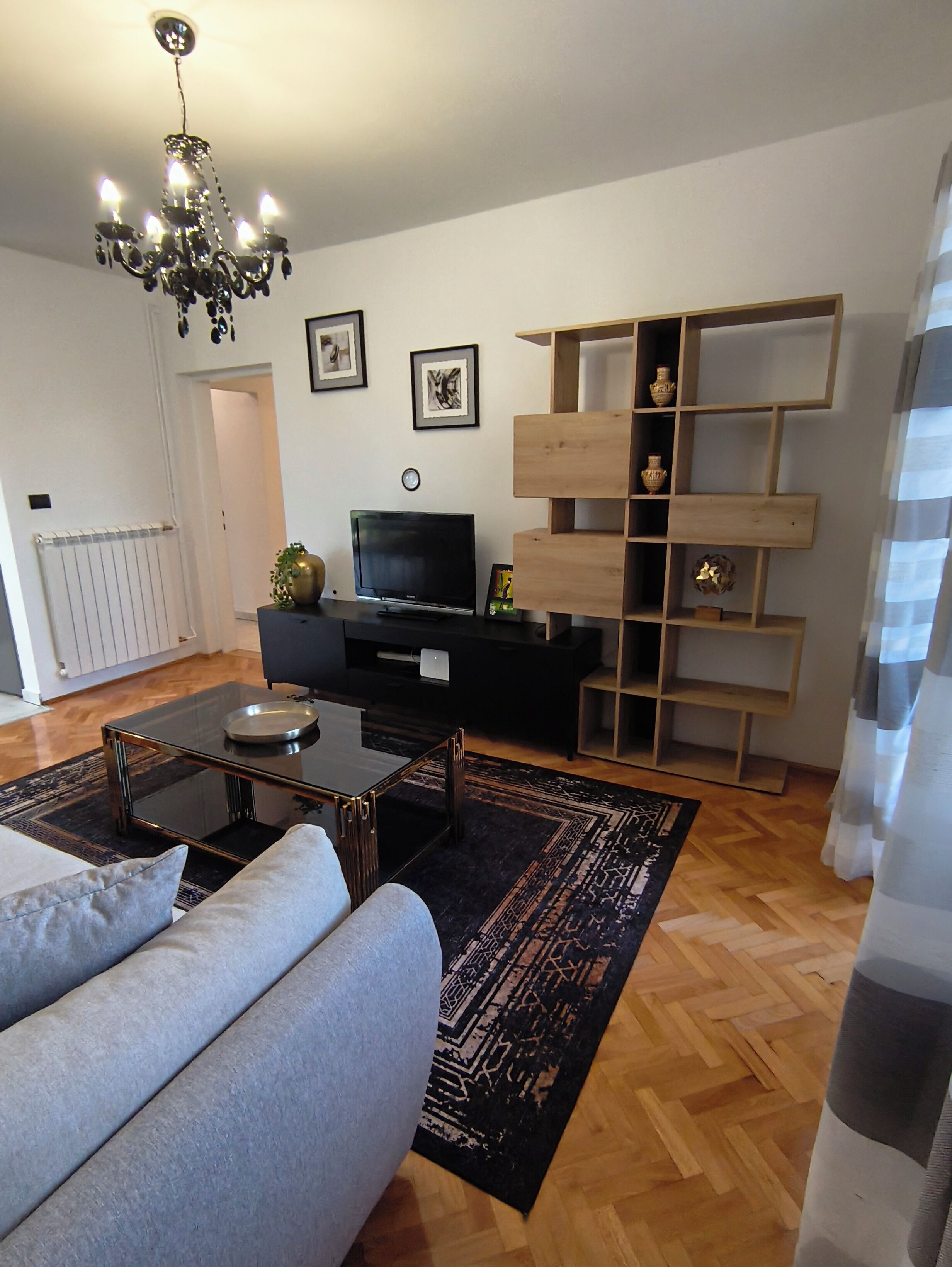 A modern living room with a sofa, a coffee table, a TV, and a wooden shelving unit.