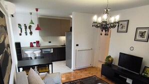 A modern living room with a sofa, a coffee table, and a TV. There is a kitchen in the background with a refrigerator and a dining area. - Apartment Zora - 
Charming 2-bedroom apartment with AC, WiFi in amazing Pula (Pula)