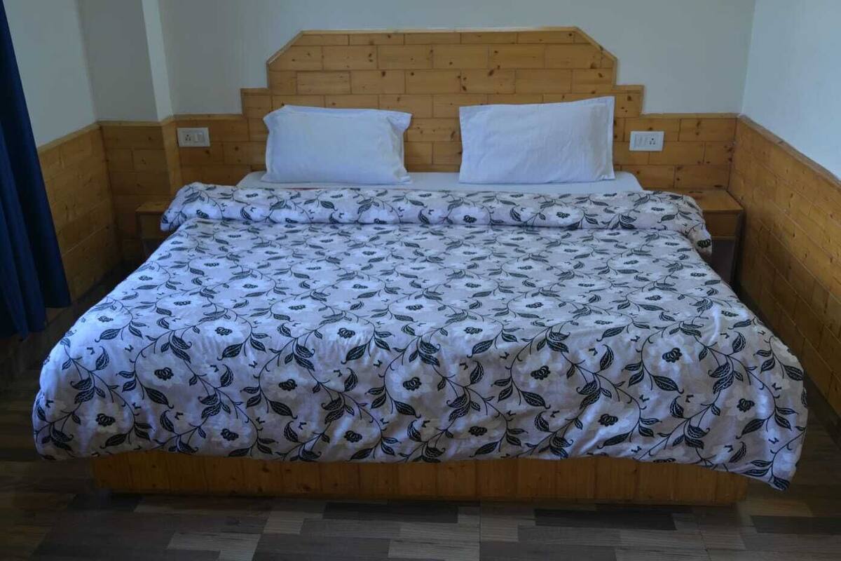 Una cama con una colcha estampada con motivos florales, un cabecero de madera y dos almohadas blancas.