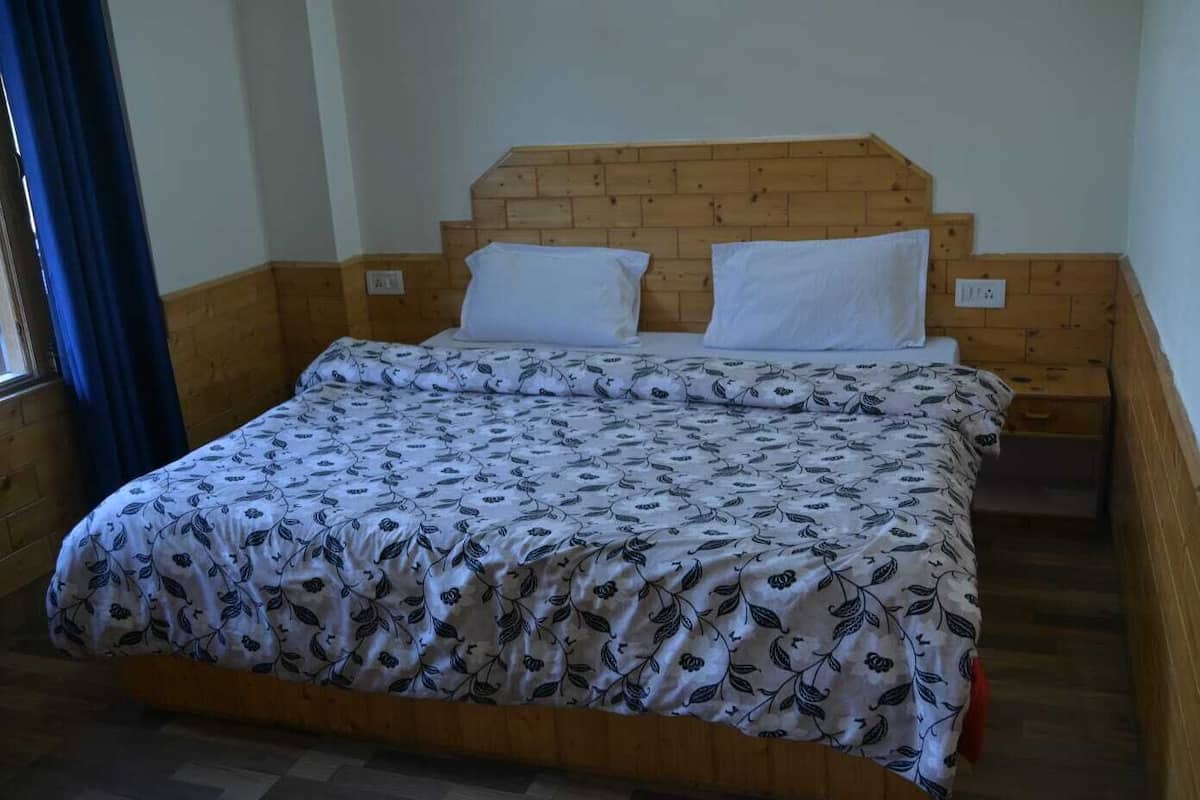 Una cama individual con una colcha estampada con motivos florales, cabecera de madera y dos almohadas blancas.