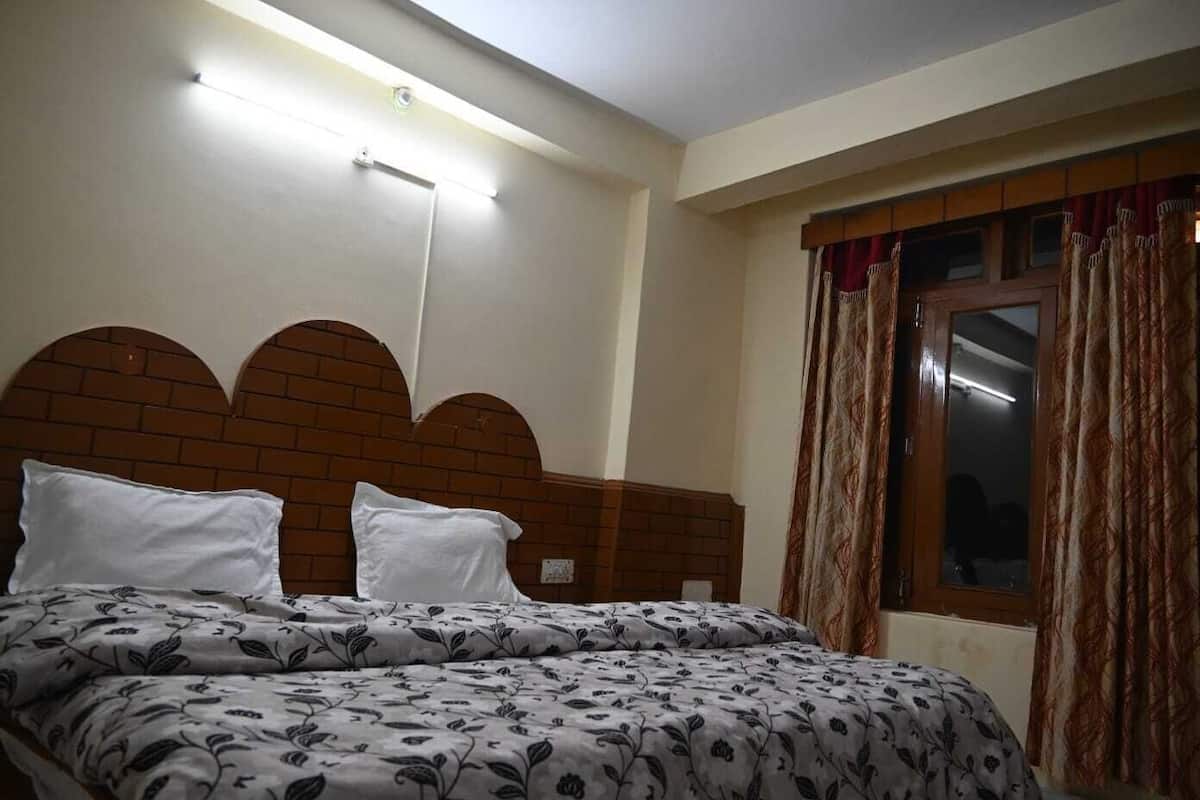 Un dormitorio con cabecera de ladrillo, una cama con ropa de cama floral, una ventana con cortinas y una lámpara en el techo.