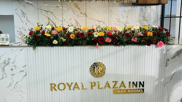 A reception desk at the Royal Plaza Inn with a marble backdrop, a chandelier, and a floral arrangement.