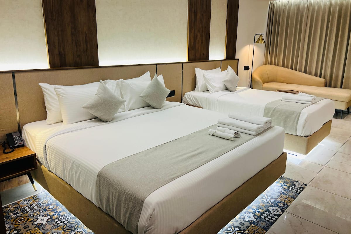 Habitación de hotel con dos camas, un sofá, una mesita de noche con teléfono y suelo estampado.