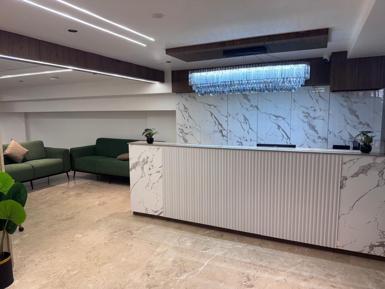 A reception area with a marble counter, green sofas, and a chandelier.