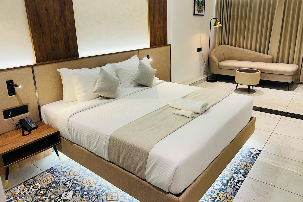 Habitación de hotel con una cama grande, una mesita de noche con teléfono, un sofá, una lámpara y una alfombra estampada.