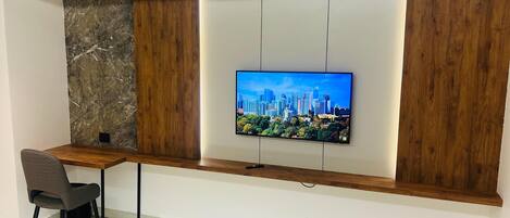 A modern office space with a desk, chair, and a large flat-screen TV mounted on a wall with wooden paneling and a cityscape image.