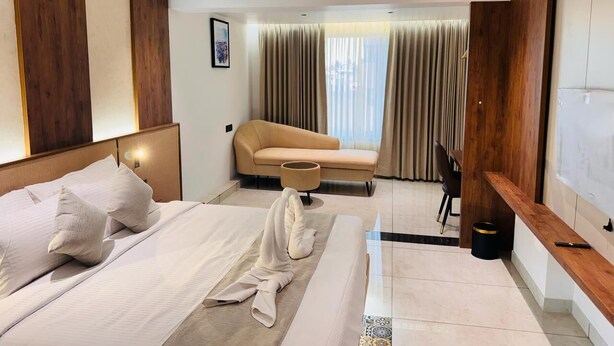 Hotellihuone, jossa on suuri sänky, sohva, työpöytä ja ikkunasta avautuva näkymä kaupunkiin.