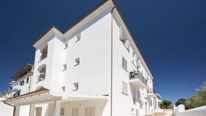 A white multi-story building with balconies, a covered patio area, and a clear sky.