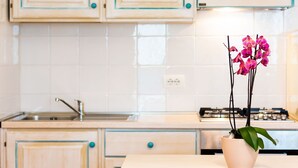 A kitchen with wooden cabinets, a sink, and a stove. There is a potted orchid on the counter.