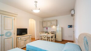 A compact room with a bed, a desk, a television, and a kitchenette.