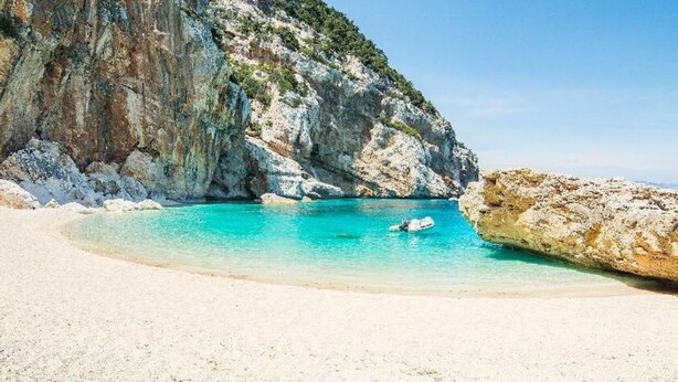 Una playa con agua turquesa cristalina, arena blanca y acantilados rocosos.