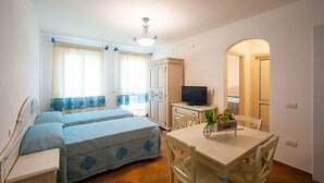 Una habitación compacta con dos camas, una mesita con frutero, un televisor y un espejo.
