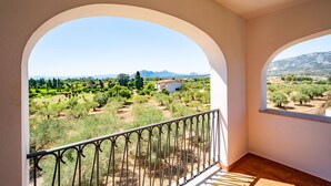 Un balcón con vistas a un paisaje rural, con árboles y una cadena montañosa distante.