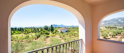 A balcony with a view of a rural landscape, including trees and a distant mountain range.