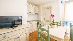 Cocina compacta con armarios blancos, una mesa de comedor y un televisor.