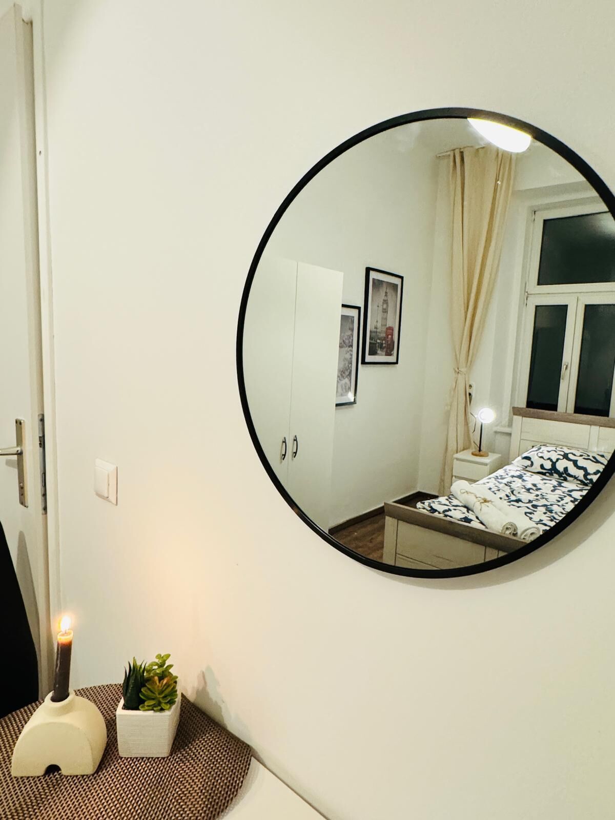 Une chambre avec un lit, une table de chevet avec une lampe, une petite plante en pot et un miroir fixé au mur.