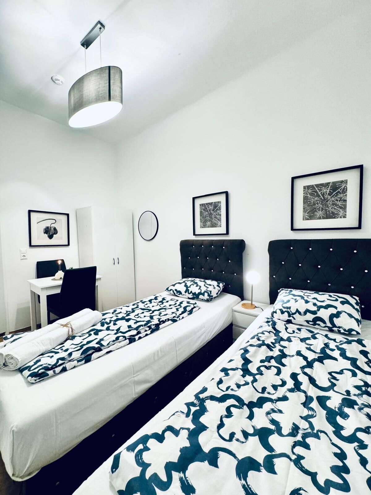 Une chambre d’hôtel avec deux lits, un bureau, une chaise et un miroir rond.