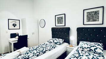 Une chambre d’hôtel avec deux lits, un bureau, une chaise et un miroir rond.