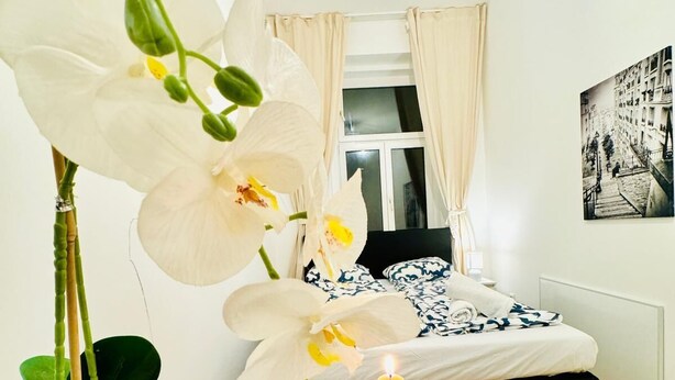 A bedroom with a bed, a nightstand, a potted orchid, and a candle. - 5BR Apt For 10 Walk to Kaufpark Alterlaa (Vienna)