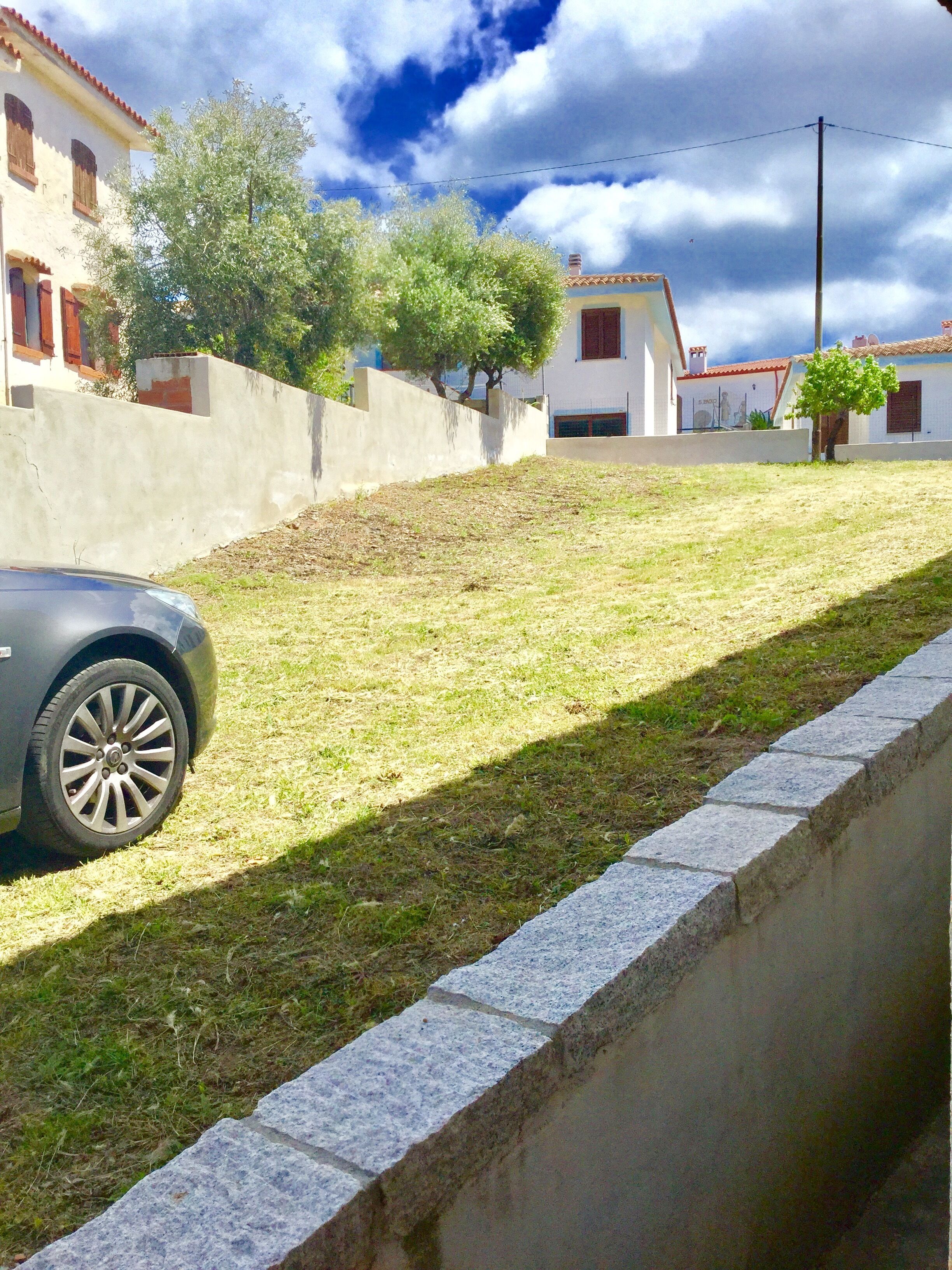 Zona residencial amb pendent herbós, mur de formigó i un cotxe estacionat.