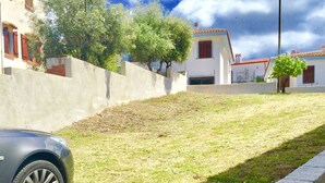 A residential area with a grassy slope, a concrete retaining wall, and a parked car.