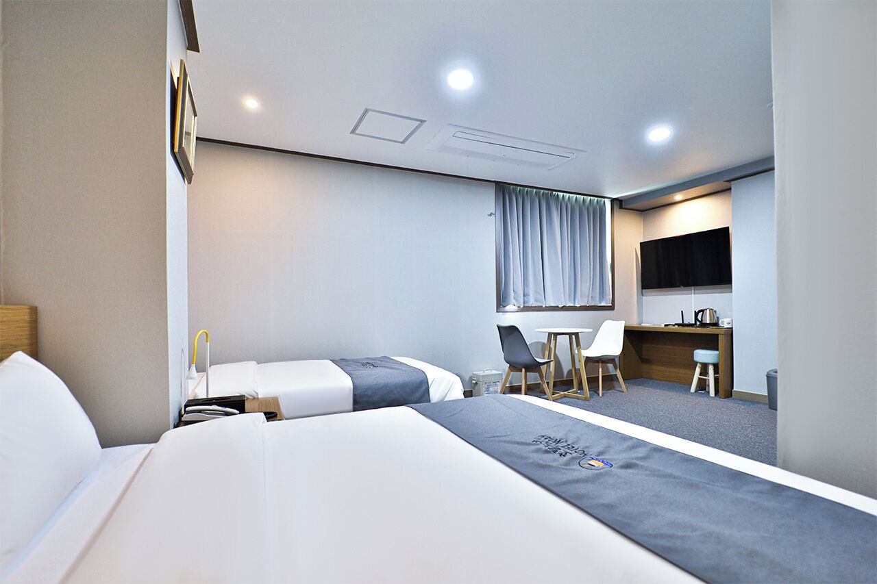 A hotel room with two beds, a desk, a chair, a TV, and a window with curtains.