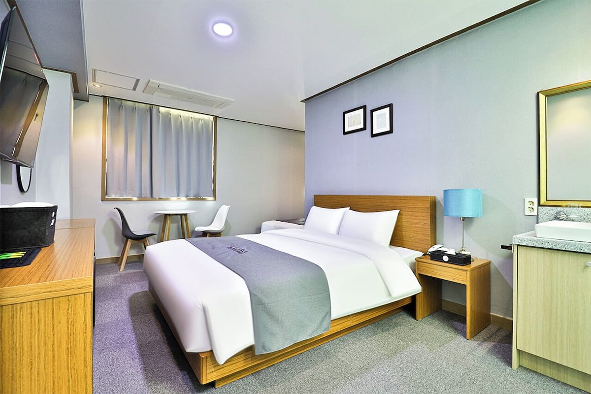 Una habitación de hotel con cama, mesita de noche, escritorio, silla y televisor.