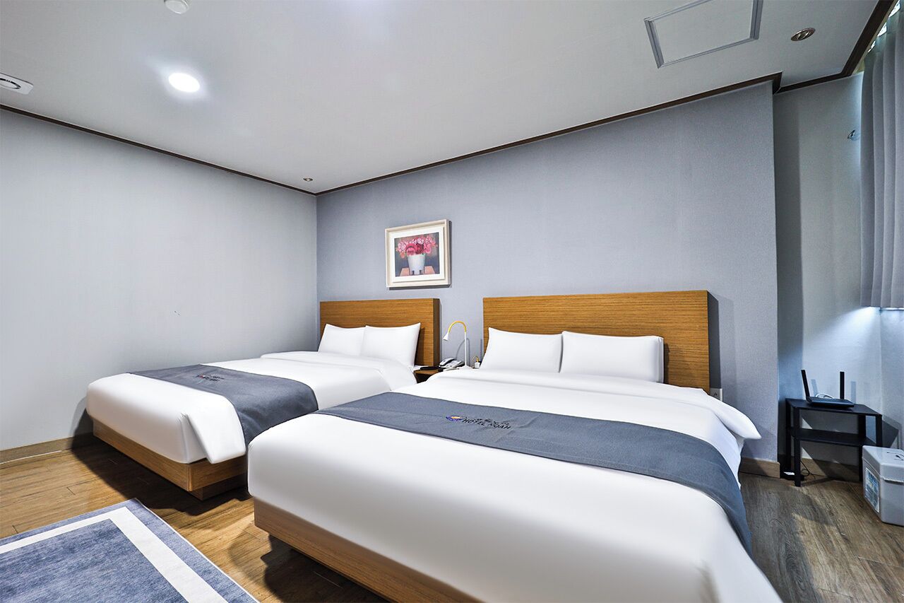 Une chambre d’hôtel moderne avec deux lits simples, une tête de lit en bois, une table de chevet avec une lampe et un tableau au mur.