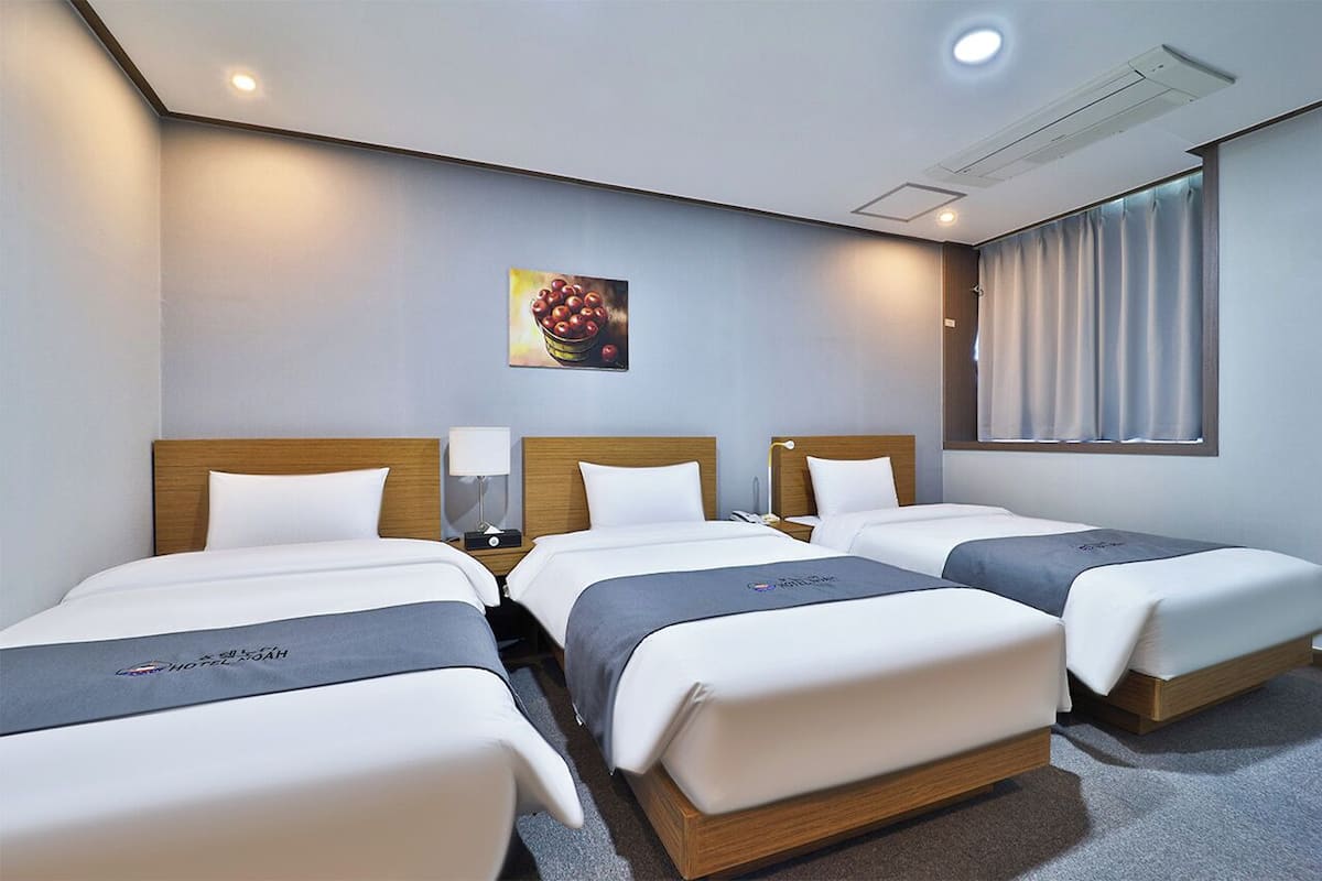 Una habitación de hotel con tres camas, un cuadro en la pared y una ventana con cortinas.