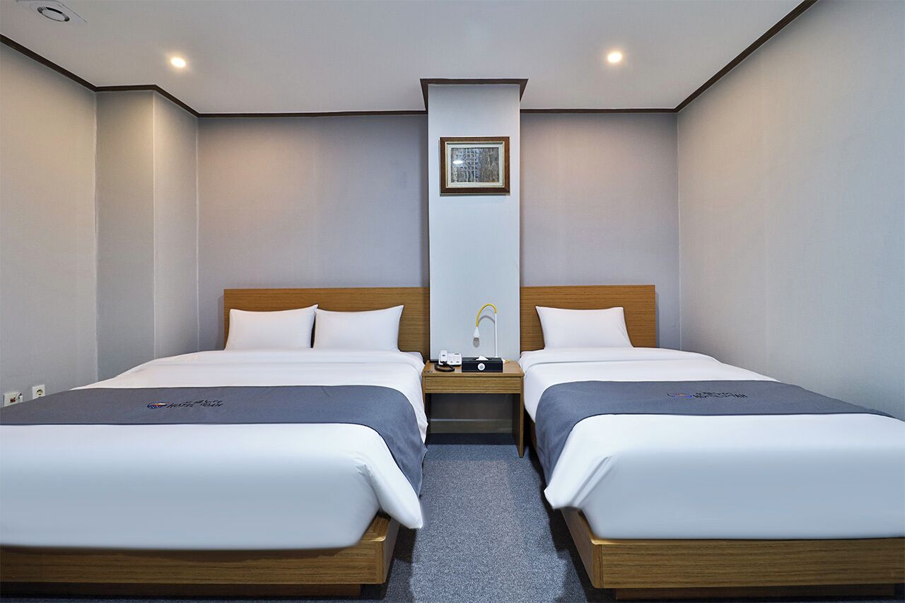 Une chambre d’hôtel avec deux lits, une tête de lit en bois, une table de chevet avec une lampe et un tableau encadré au mur.