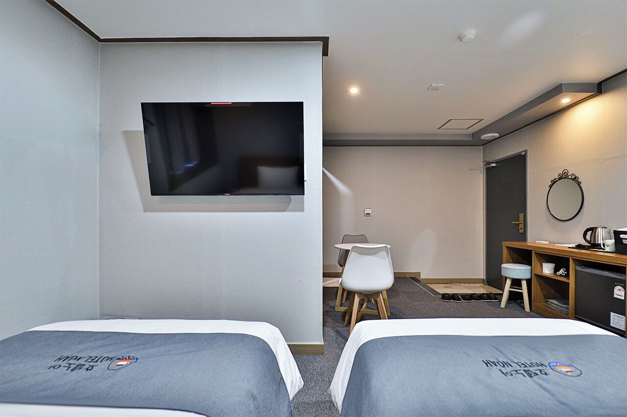 Ein Hotelzimmer mit zwei Betten, einem an der Wand befestigten Fernseher, einem Schreibtisch mit Stuhl und einem Wandspiegel.