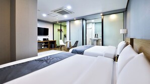 Ein Hotelzimmer mit zwei Betten, einem Schreibtisch, einem Sessel, einem Fernseher und einem Fenster.