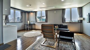 Ein modernes Hotelzimmer mit großem Fenster, einer Couch, einem Sessel, einem kleinen Tisch und einer Dekovase.